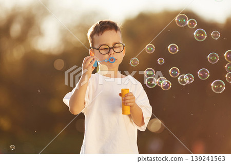 Blowing bubbles. Boy is having fun on the field under sunlight at daytime 139241563