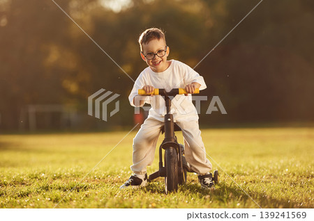 On the small bicycle. Boy is having fun on the field under sunlight at daytime 139241569