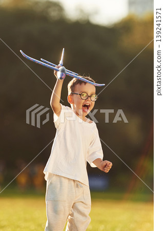 Toy plane is in hand, high up. Boy is having fun on the field under sunlight at daytime Toy plane is in hand, high up. Boy is having fun on the field under sunlight at daytime 139241571