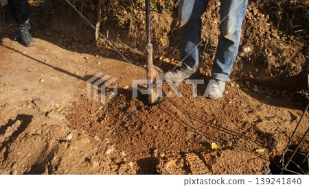 installing solar fence posts in open landscape, using auger to install solar fence posts in dusty terrain, installer using auger to set posts for solar fencing amidst bright sun and open installing solar fence posts in open landscape, using auger to install solar fence posts in dusty terrain, installer using auger to set posts for solar fencing amidst bright sun and open 139241840