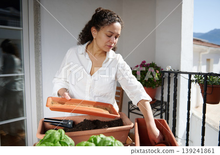 Woman Gardening on Balcony Planting Herbs in Pots and Planters in Sunny Urban Home Woman Gardening on Balcony Planting Herbs in Pots and Planters in Sunny Urban Home 139241861