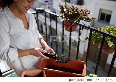 Smiling Woman Planting Soil in Balcony Planter While Gardening on Urban Terrace Smiling Woman Planting Soil in Balcony Planter While Gardening on Urban Terrace 139241870