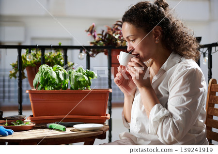 Woman Drinking Coffee on Balcony While Tending Potted Basil Plants in Morning Urban Garden Woman Drinking Coffee on Balcony While Tending Potted Basil Plants in Morning Urban Garden 139241919