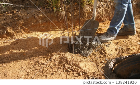 worker uses sturdy boots, worker employs durable boots for soil, worker utilizes solid boots to pack soil firmly, worker relies on tough boots to securely compact soil around posts 139241920