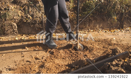 worker drills hole, heavyduty boots assist in drilling task, worker with boots rotates auger to create post hole, utility worker in heavy boots drills into earth using rotating auger device 139241922