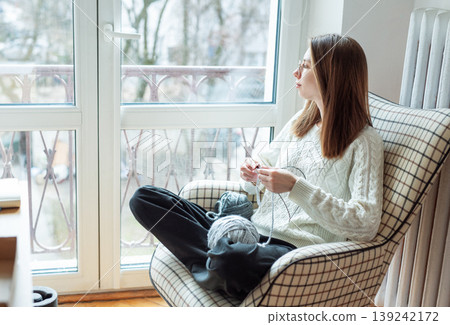Woman knitting yarn looking out window relaxing Woman knitting yarn looking out window relaxing 139242172