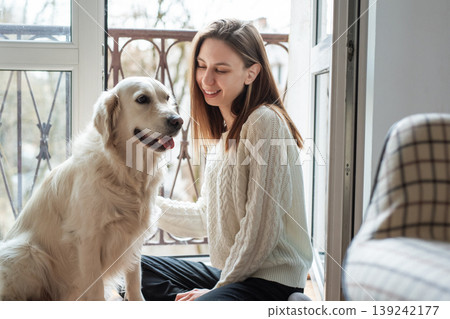 Woman smiling and petting golden retriever dog on balcony Woman smiling and petting golden retriever dog on balcony 139242177