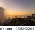 The sea and cityscape are bathed in the colors of the setting sun, creating a beautiful silhouette and a tranquil twilight scene. 139242204