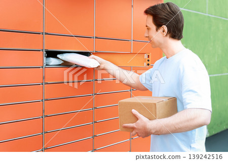 A man picks up a parcel from an automated delivery locker. Concept of ecommerce, shopping, and shipping services using a modern package terminal station. A man picks up a parcel from an automated delivery locker. Concept of ecommerce, shopping, and shipping services using a modern package terminal station. 139242516