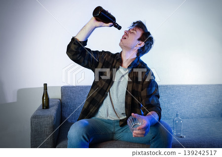 Man struggling with alcoholism and addiction, drinking alone on a couch. Concepts of unemployment, depression, and loneliness after a painful divorce or separation. 139242517