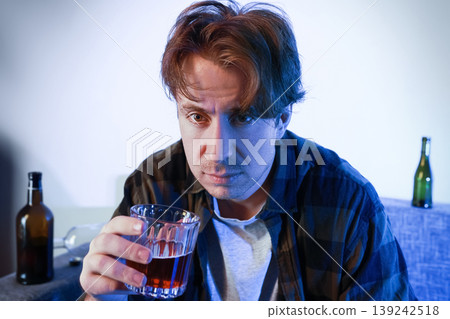 Depressed man with alcoholism and addiction holding a glass of liquor. Depicting the pain of divorce, unemployment, and separation through solitary drunkenness. 139242518