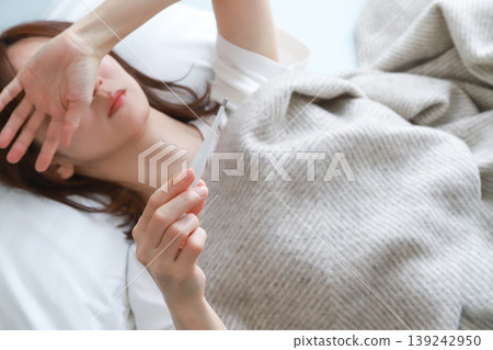 A woman sleeping in bed with a thermometer. A woman sleeping in bed with a thermometer. 139242950