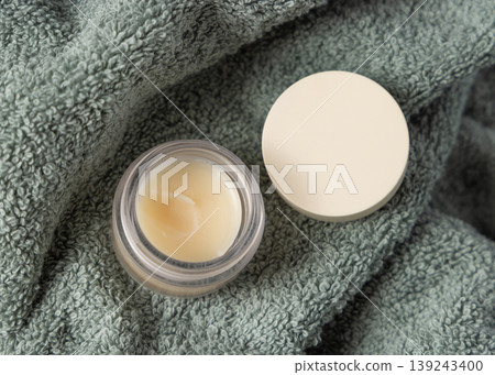 Opened handmade lip balm jar with blank lid mockup on light green bath towel. Unbranded packaging Opened handmade lip balm jar with blank lid mockup on light green bath towel. Unbranded packaging 139243400
