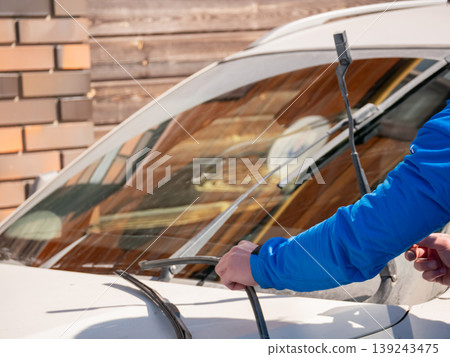 Man changing windshield wiper blade on car. Mechanic replacing broken auto part. Vehicle maintenance and repair service. Automotive diagnostic and preparation for driving in rain and storm. 139243475