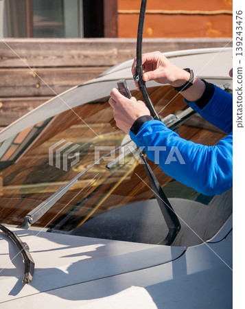 Man changing windshield wiper blade on car. Mechanic replacing broken auto part. Vehicle maintenance and repair service. Automotive diagnostic and preparation for driving in rain and storm. Man changing windshield wiper blade on car. Mechanic replacing broken auto part. Vehicle maintenance and repair service. Automotive diagnostic and preparation for driving in rain and storm. 139243476