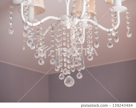 White chandelier with hanging crystal glass pendants. Elegant interior ceiling lighting for home decor. Decorative lamp with gem-like refraction for luxury room design and living space. White chandelier with hanging crystal glass pendants. Elegant interior ceiling lighting for home decor. Decorative lamp with gem-like refraction for luxury room design and living space. 139243484