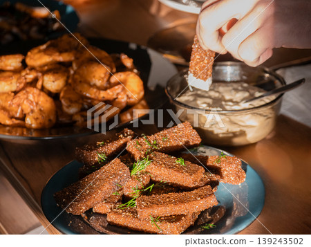 Man dipping rye bread crouton into sauce. Hand taking crispy garlic bread appetizer from plate. Table with shrimp and snack for social gathering or home party dinner culinary concept. Man dipping rye bread crouton into sauce. Hand taking crispy garlic bread appetizer from plate. Table with shrimp and snack for social gathering or home party dinner culinary concept. 139243502