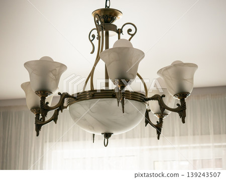 Antique brass chandelier with frosted glass shades hanging from ceiling. Elegant vintage light fixture for interior home decoration. Luxurious lighting design for classic room style. Antique brass chandelier with frosted glass shades hanging from ceiling. Elegant vintage light fixture for interior home decoration. Luxurious lighting design for classic room style. 139243507
