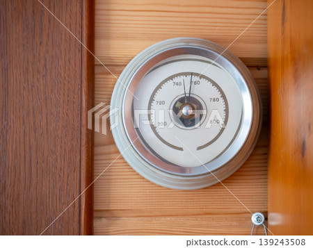 Barometer mounted on a wooden wall. Analog atmospheric pressure gauge showing regular weather data. Classic instrument for meteorological monitoring and climate study in home interior. 139243508