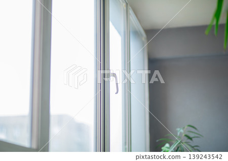 White window frame in interior. Modern glass architecture with handle in room. Transparent glazing for bright residential house. Energy efficient construction and home renovation concept. White window frame in interior. Modern glass architecture with handle in room. Transparent glazing for bright residential house. Energy efficient construction and home renovation concept. 139243542