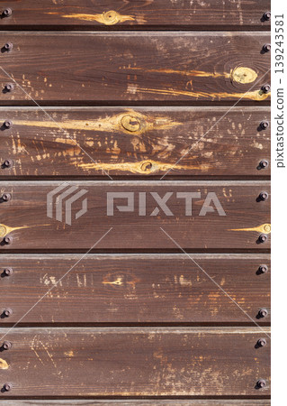 Dark brown wooden planks wall with metal bolts background. Rustic building exterior facade with natural grain pattern. Industrial construction material texture for interior design background. Dark brown wooden planks wall with metal bolts background. Rustic building exterior facade with natural grain pattern. Industrial construction material texture for interior design background. 139243581
