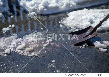 Metal shovel clearing slush and snow from sidewalk. Manual labor task during winter season. Maintenance work in cold weather conditions and icy environment for safety and winter cleanup. Metal shovel clearing slush and snow from sidewalk. Manual labor task during winter season. Maintenance work in cold weather conditions and icy environment for safety and winter cleanup. 139243596