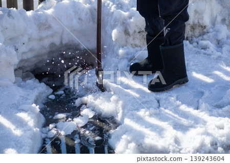Man breaking ice with ice pick on sidewalk. Winter street snow removal and maintenance. Worker clearing frozen path surface. Safe movement during cold season and icy road conditions. Man breaking ice with ice pick on sidewalk. Winter street snow removal and maintenance. Worker clearing frozen path surface. Safe movement during cold season and icy road conditions. 139243604