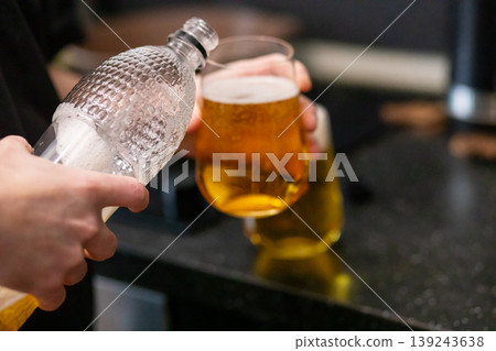Person pouring refreshing lager beer from glass bottle into glass. Alcohol drink served for party celebration. Fresh beverage with foam bubbles in pub night environment. Pub culture. Person pouring refreshing lager beer from glass bottle into glass. Alcohol drink served for party celebration. Fresh beverage with foam bubbles in pub night environment. Pub culture. 139243638