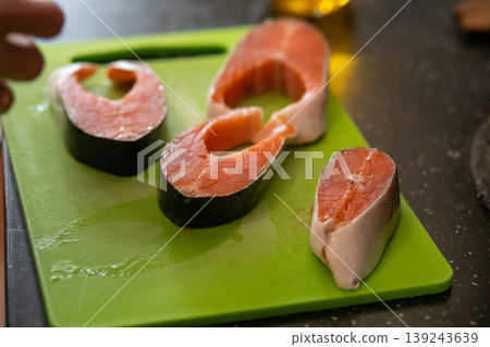 Raw salmon steak seasoned with pepper on green cutting board. Preparation of fish for cooking dinner. Healthy seafood diet and culinary concept for kitchen and home food ingredient. Raw salmon steak seasoned with pepper on green cutting board. Preparation of fish for cooking dinner. Healthy seafood diet and culinary concept for kitchen and home food ingredient. 139243639