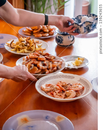 Woman serving shrimp on table. Family dinner with seafood and appetizer plates. Preparing dining meal for celebration. Home cooking and gathering, eating together, domestic lifestyle event. Woman serving shrimp on table. Family dinner with seafood and appetizer plates. Preparing dining meal for celebration. Home cooking and gathering, eating together, domestic lifestyle event. 139243655