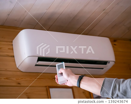 Man using remote control to turn on air conditioner mounted on wall. Person adjusting climate control settings for comfortable indoor temperature. Modern home cooling and heating system. Man using remote control to turn on air conditioner mounted on wall. Person adjusting climate control settings for comfortable indoor temperature. Modern home cooling and heating system. 139243674