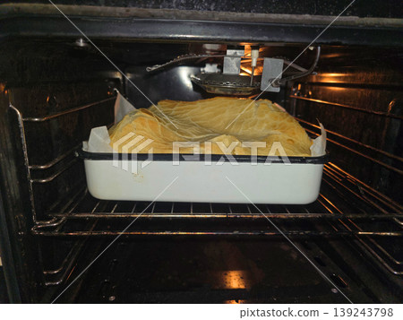 Puff pastry baking in oven on metal tray. Golden crispy crust of homemade pie cooking inside kitchen appliance. Culinary process of preparing delicious dessert or savory pastry snack meal. Puff pastry baking in oven on metal tray. Golden crispy crust of homemade pie cooking inside kitchen appliance. Culinary process of preparing delicious dessert or savory pastry snack meal. 139243798