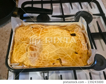 Homemade meat pie in baking tray on stove. Golden crispy puff pastry crust covering savory dish. Freshly baked meal cooling down in kitchen. Rustic style culinary concept for dinner. Homemade meat pie in baking tray on stove. Golden crispy puff pastry crust covering savory dish. Freshly baked meal cooling down in kitchen. Rustic style culinary concept for dinner. 139243800
