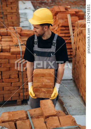 In gray uniform, standing. A builder is working at the construction site at daytime In gray uniform, standing. A builder is working at the construction site at daytime 139243881