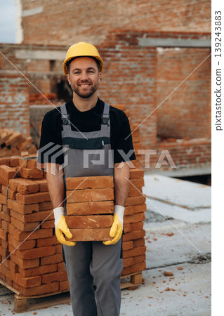 The bricks in hands, holding it. A builder is working at the construction site at daytime 139243883