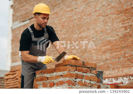 Placing the bricks, making a wall. A builder is working at the construction site at daytime 139243902