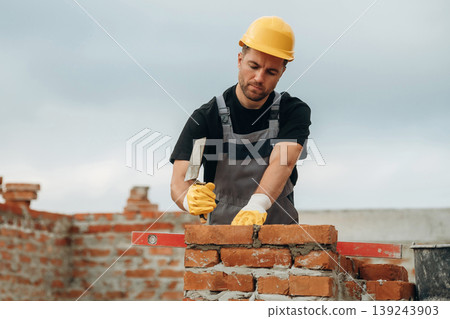 Placing the bricks, making a wall. A builder is working at the construction site at daytime Placing the bricks, making a wall. A builder is working at the construction site at daytime 139243903