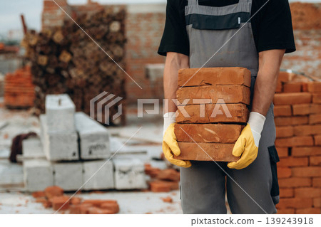 Many of the bricks are in hands. Close up view of builder that is on the construction site Many of the bricks are in hands. Close up view of builder that is on the construction site 139243918