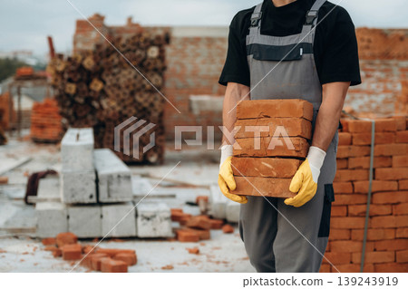 Many of the bricks are in hands. Close up view of builder that is on the construction site Many of the bricks are in hands. Close up view of builder that is on the construction site 139243919