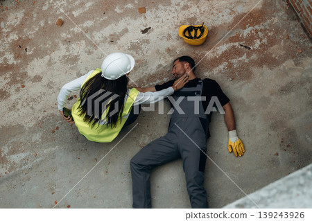 Top view. Man, construction worker fell from big height, lying down without consciousness, accident, woman is checking Top view. Man, construction worker fell from big height, lying down without consciousness, accident, woman is checking 139243926