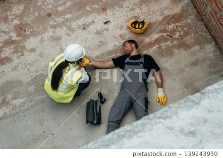 Top view. Man, construction worker fell from big height, lying down without consciousness, accident, woman is checking 139243930