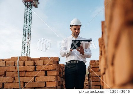 Writing information into notepad. A builder is working at the construction site at daytime Writing information into notepad. A builder is working at the construction site at daytime 139243946