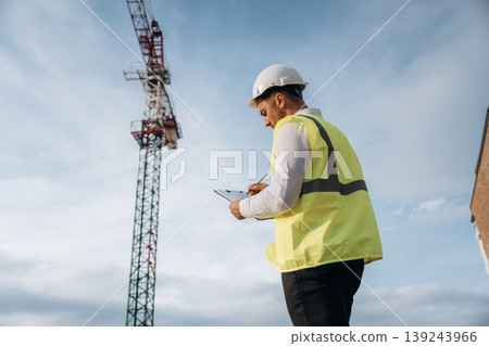 According to a plan. Construction site worker is against building crane and sky background According to a plan. Construction site worker is against building crane and sky background 139243966