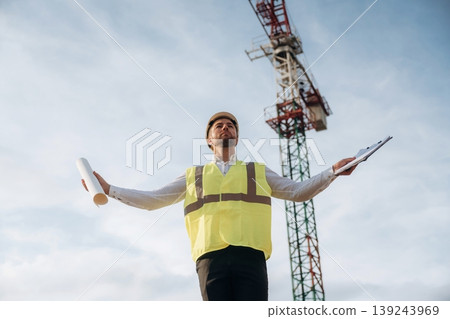 According to a plan. Construction site worker is against building crane and sky background According to a plan. Construction site worker is against building crane and sky background 139243969