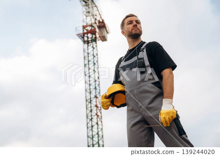 Break time, standing and posing. Construction site worker is against building crane and sky background Break time, standing and posing. Construction site worker is against building crane and sky background 139244020