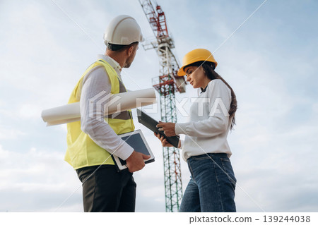 Man and woman, construction site workers are against crane, communication 139244038