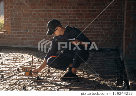 Sitting and using leveling tool. Builder is working on construction site, unfinished building 139244232