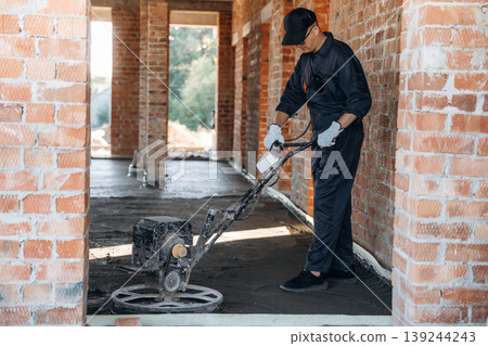 Process of leveling the concrete on the floor. Builder is working on construction site, unfinished building Process of leveling the concrete on the floor. Builder is working on construction site, unfinished building 139244243