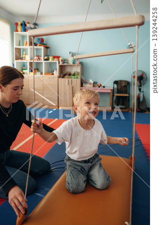 Balancing on the surface that is swinging. Preschool child with teacher during developmental activities in a playroom 139244258