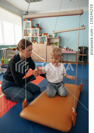 Balancing on the surface that is swinging. Preschool child with teacher during developmental activities in a playroom 139244259